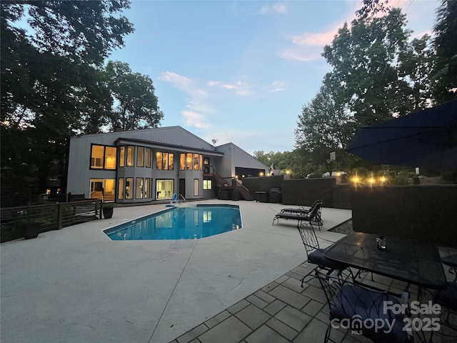 pool at dusk featuring a fenced in pool, fence, stairway, and a patio area