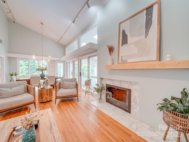 living room featuring visible vents, a premium fireplace, light wood-style flooring, rail lighting, and high vaulted ceiling