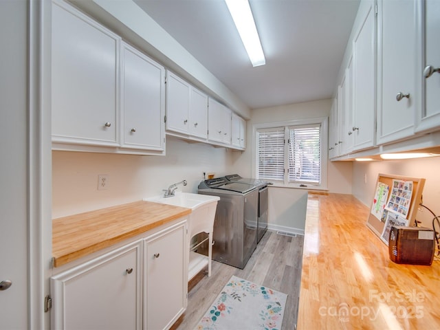 washroom featuring light wood-style flooring, cabinet space, baseboards, and washer and clothes dryer