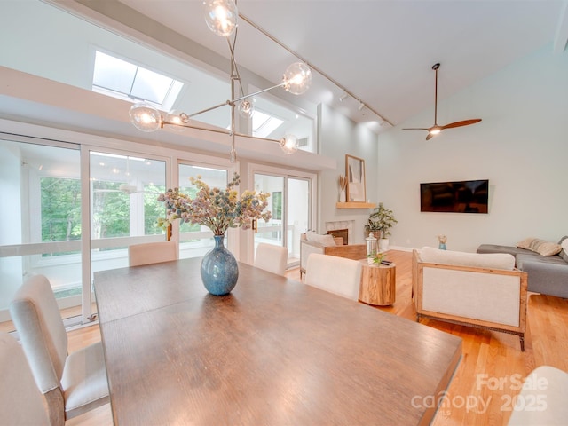 dining space featuring a ceiling fan, high vaulted ceiling, a skylight, light wood-style flooring, and rail lighting