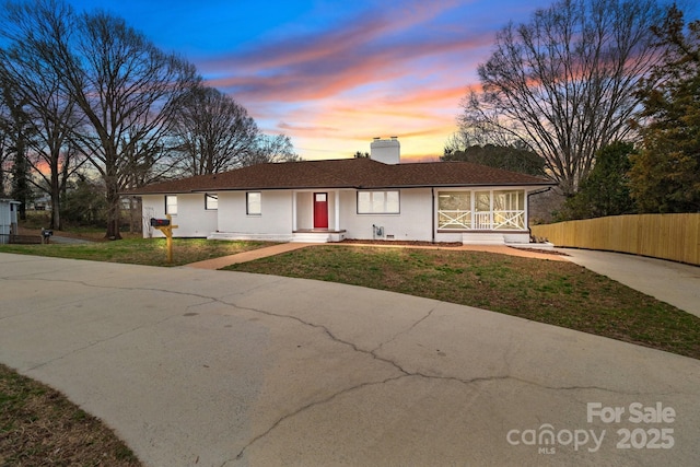 ranch-style home featuring a front yard, concrete driveway, fence, and a chimney