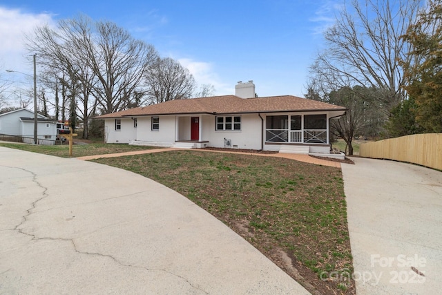 ranch-style home with a front lawn, a sunroom, fence, a shingled roof, and a chimney