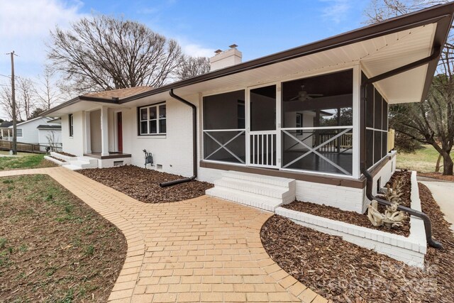 view of front facade with crawl space, a chimney, brick siding, and a sunroom