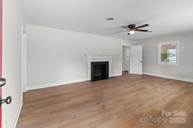 unfurnished living room featuring wood finished floors, visible vents, baseboards, a fireplace with flush hearth, and ceiling fan