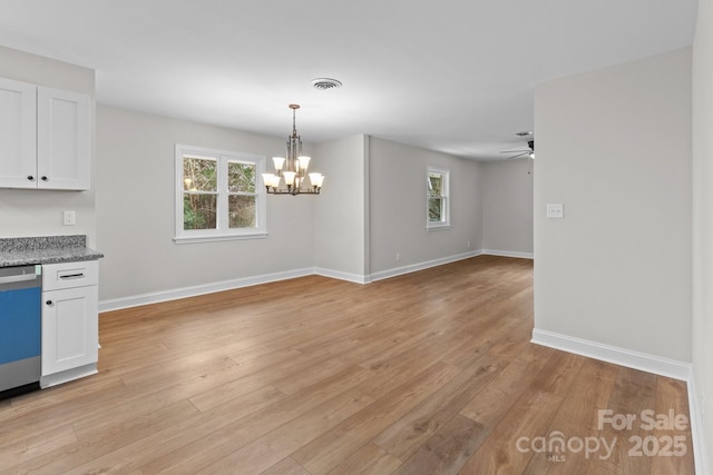 unfurnished dining area with ceiling fan with notable chandelier, light wood-style flooring, baseboards, and visible vents