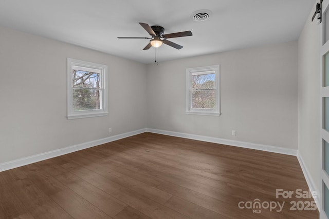 empty room with visible vents, plenty of natural light, baseboards, and dark wood finished floors