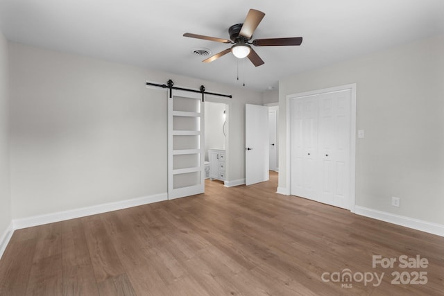 unfurnished bedroom featuring visible vents, wood finished floors, a barn door, a closet, and baseboards