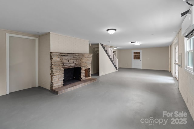 unfurnished living room featuring a stone fireplace, stairway, a wall mounted AC, and concrete floors