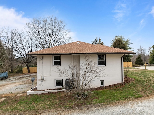 view of home's exterior with brick siding, roof with shingles, and fence