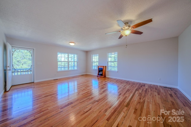 unfurnished living room with a fireplace, a textured ceiling, light wood-type flooring, and baseboards