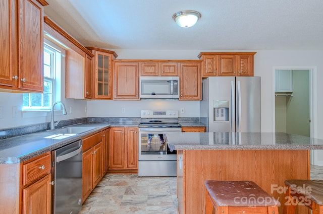 kitchen featuring a sink, a kitchen island, stainless steel appliances, brown cabinetry, and glass insert cabinets