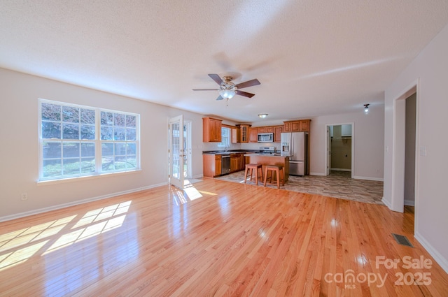 kitchen with visible vents, open floor plan, appliances with stainless steel finishes, and brown cabinets