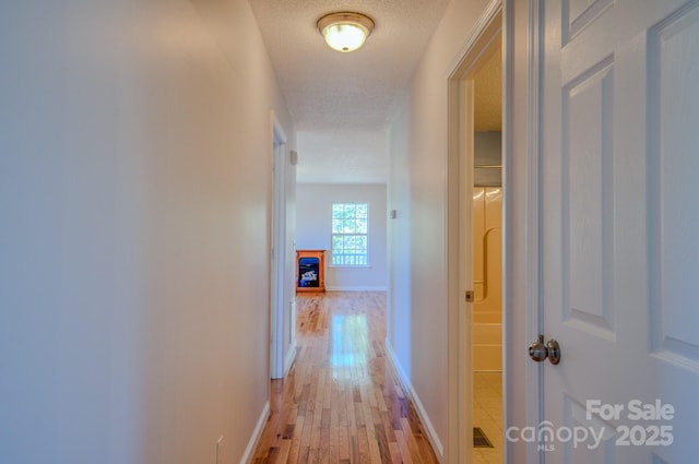 hall with light wood-style flooring, a textured ceiling, and baseboards