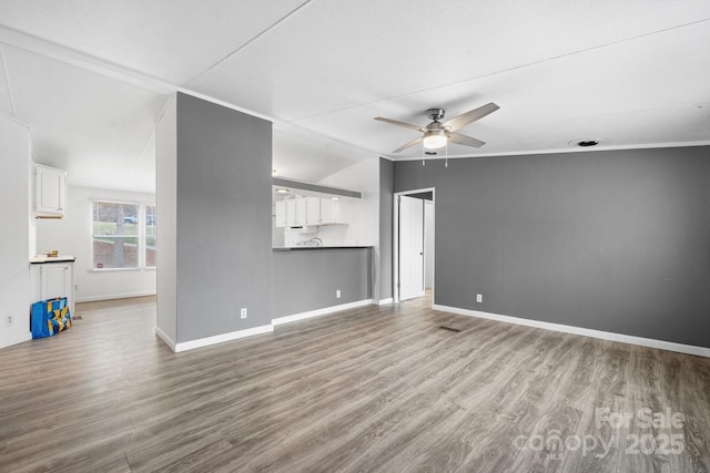 unfurnished living room featuring a ceiling fan, vaulted ceiling, wood finished floors, and baseboards