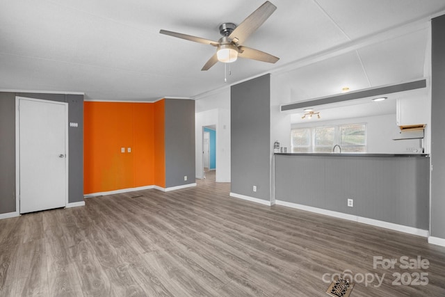 unfurnished living room with baseboards, wood finished floors, and a ceiling fan