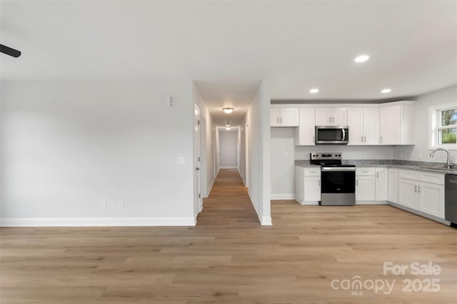 kitchen with light wood finished floors, recessed lighting, a sink, stainless steel appliances, and white cabinets