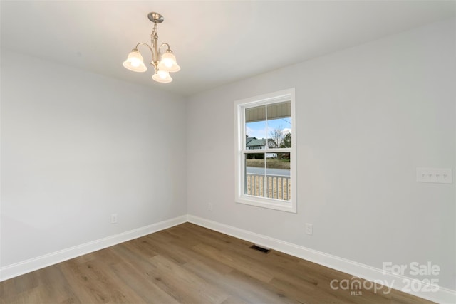 spare room featuring visible vents, a notable chandelier, wood finished floors, and baseboards