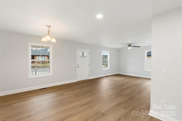 unfurnished living room featuring ceiling fan with notable chandelier, visible vents, wood finished floors, and baseboards