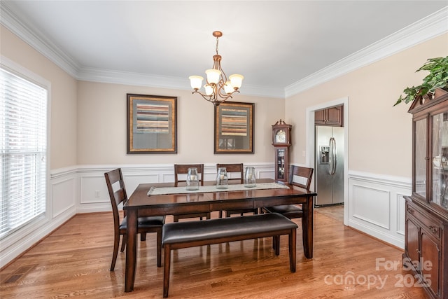 dining space featuring light wood-style floors, an inviting chandelier, wainscoting, and crown molding