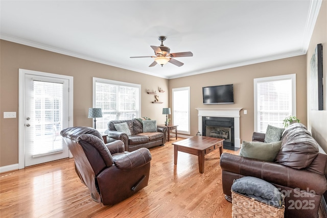 living room featuring light wood-type flooring, a fireplace with flush hearth, a ceiling fan, and crown molding