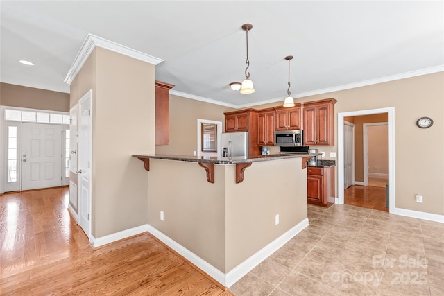 kitchen featuring dark stone counters, brown cabinets, a peninsula, a kitchen breakfast bar, and stainless steel appliances