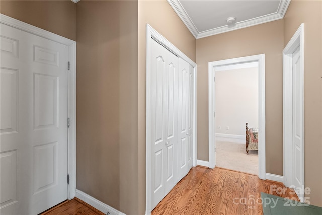 hall with light wood-type flooring, baseboards, and crown molding