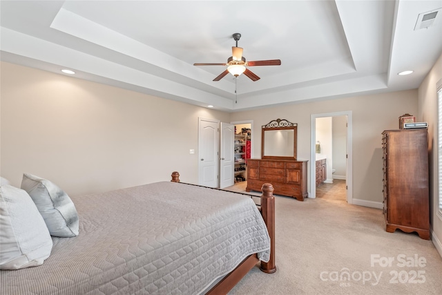 bedroom with visible vents, baseboards, a tray ceiling, a walk in closet, and light colored carpet