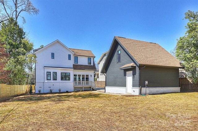 rear view of house with a shingled roof, a yard, and fence