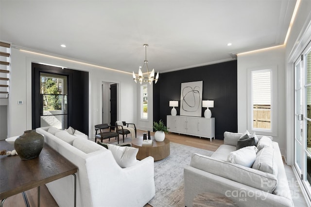 living area with a notable chandelier, a healthy amount of sunlight, ornamental molding, and wood finished floors
