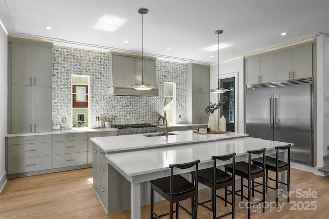 kitchen with gray cabinetry, wall chimney range hood, stainless steel built in fridge, ornamental molding, and a sink