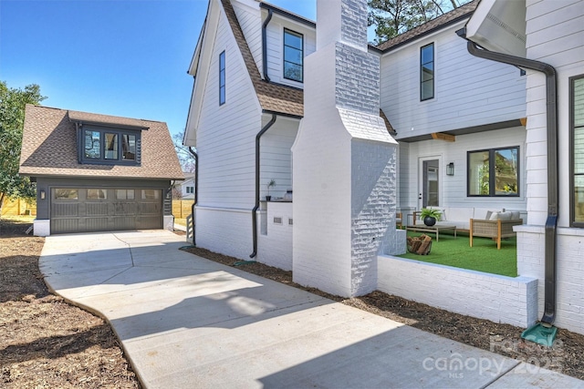 view of side of property featuring outdoor lounge area, roof with shingles, concrete driveway, and a chimney