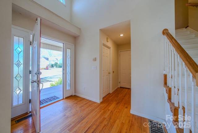 foyer entrance with light wood finished floors, visible vents, stairs, and baseboards