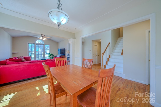 dining space with ceiling fan, stairs, vaulted ceiling, light wood-style flooring, and ornate columns