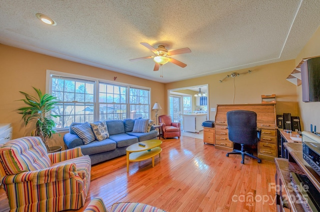 living area with a ceiling fan, light wood-type flooring, and a textured ceiling