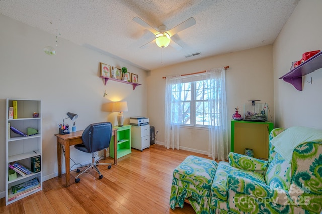 home office with a ceiling fan, wood finished floors, visible vents, and a textured ceiling