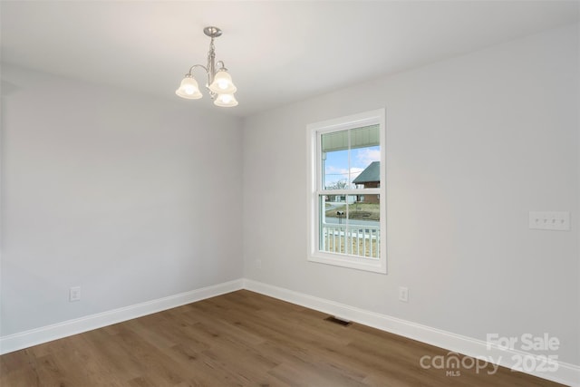 spare room featuring wood finished floors, a notable chandelier, baseboards, and visible vents