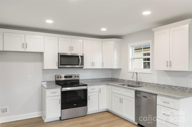 kitchen featuring white cabinets, appliances with stainless steel finishes, light wood-style flooring, and a sink