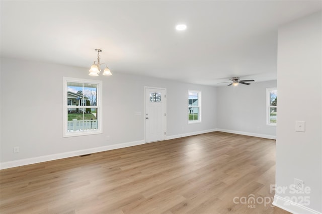 unfurnished living room featuring ceiling fan with notable chandelier, plenty of natural light, light wood-style floors, and baseboards