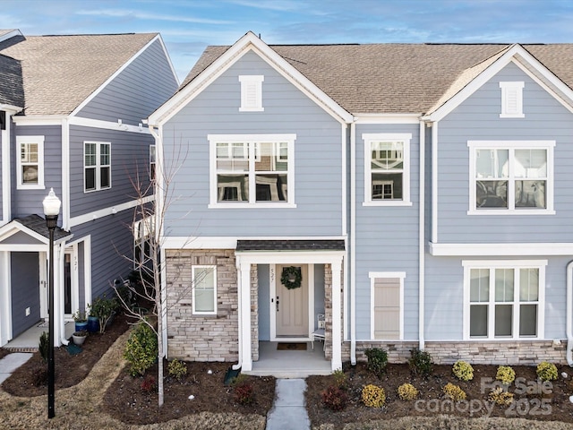 townhome / multi-family property with stone siding and a shingled roof