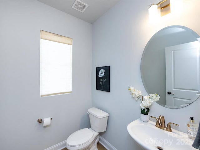 half bathroom with a sink, visible vents, baseboards, and toilet