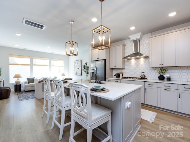 kitchen with visible vents, a breakfast bar, backsplash, stainless steel appliances, and wall chimney exhaust hood