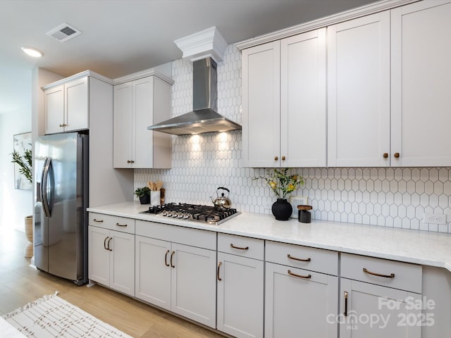 kitchen with visible vents, light wood-style flooring, appliances with stainless steel finishes, wall chimney exhaust hood, and backsplash