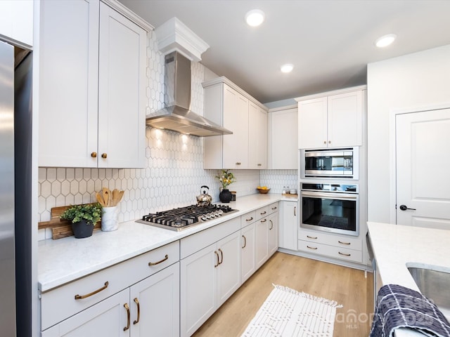 kitchen with tasteful backsplash, recessed lighting, light wood-style floors, appliances with stainless steel finishes, and wall chimney exhaust hood