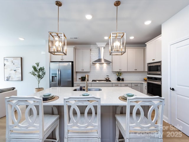 kitchen featuring backsplash, wall chimney range hood, a kitchen breakfast bar, stainless steel appliances, and a sink