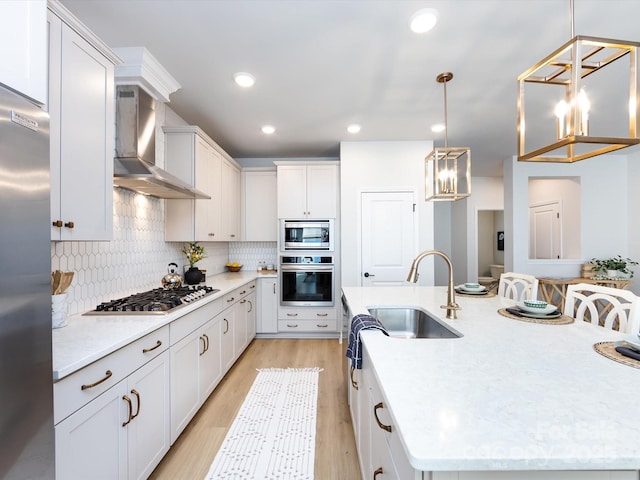 kitchen with a sink, appliances with stainless steel finishes, wall chimney exhaust hood, decorative backsplash, and a large island with sink