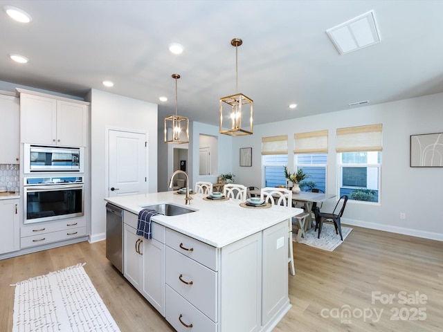 kitchen featuring light wood-style flooring, a sink, tasteful backsplash, appliances with stainless steel finishes, and light countertops