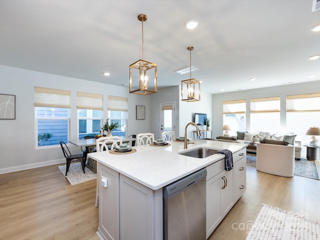 kitchen featuring a sink, dishwasher, light countertops, light wood-style floors, and a kitchen island with sink