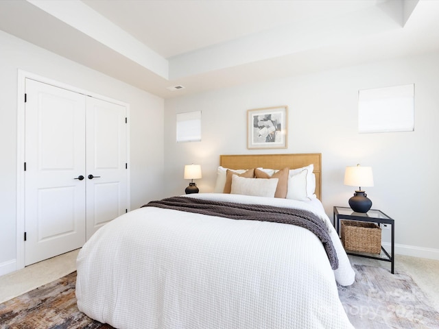 bedroom featuring visible vents, a tray ceiling, a closet, baseboards, and light colored carpet