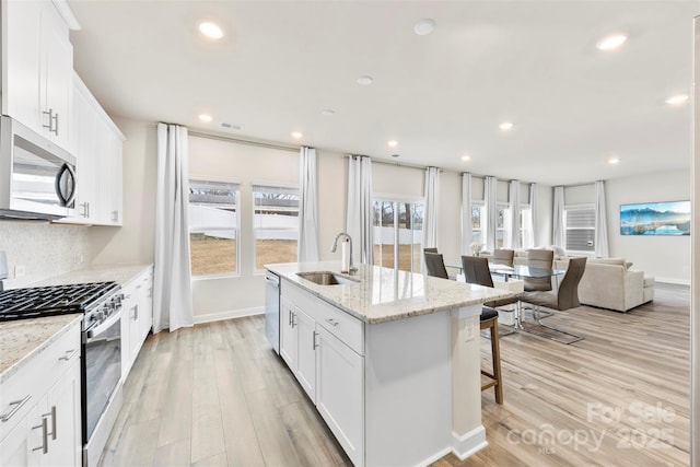 kitchen with an island with sink, light wood-style flooring, a kitchen breakfast bar, stainless steel appliances, and a sink