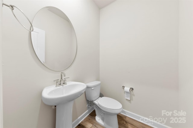 half bathroom with toilet, wood finished floors, and baseboards